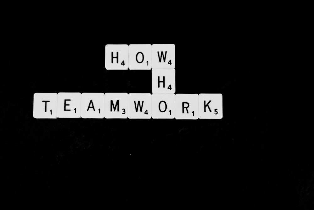 Una foto en blanco y negro de fichas de Scrabble que deletrean la palabra trabajo en equipo