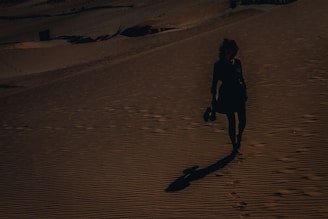 woman in black jacket walking on brown sand during daytime
