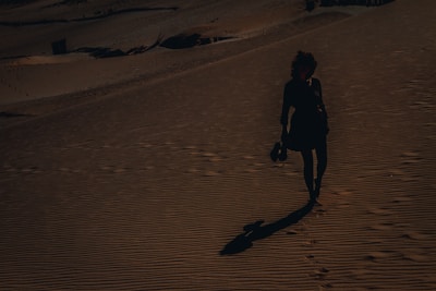 woman in black jacket walking on brown sand during daytime