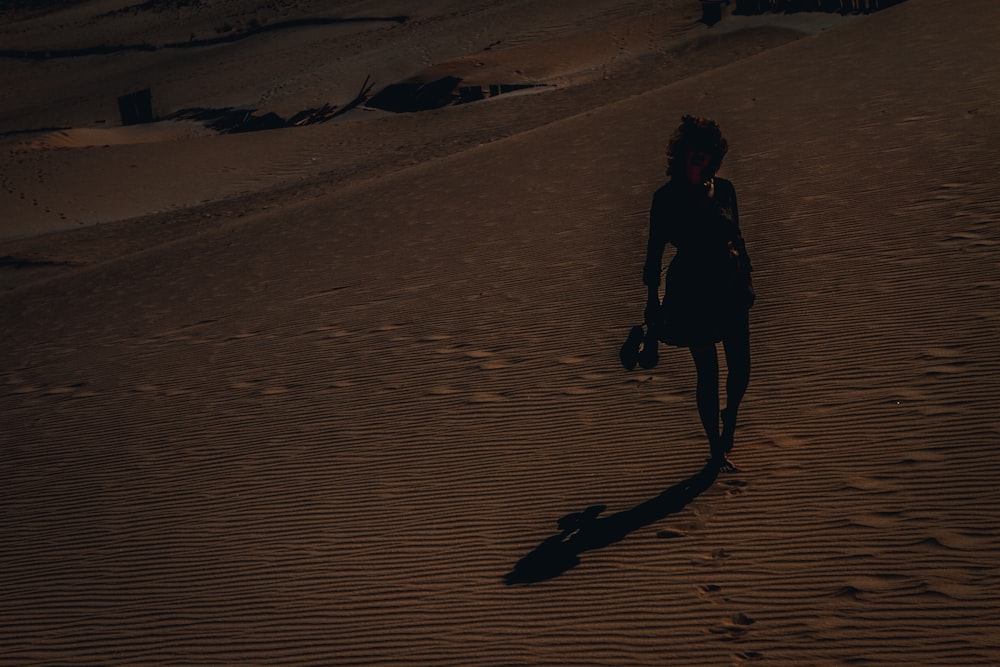 Mujer con chaqueta negra caminando sobre arena marrón durante el día