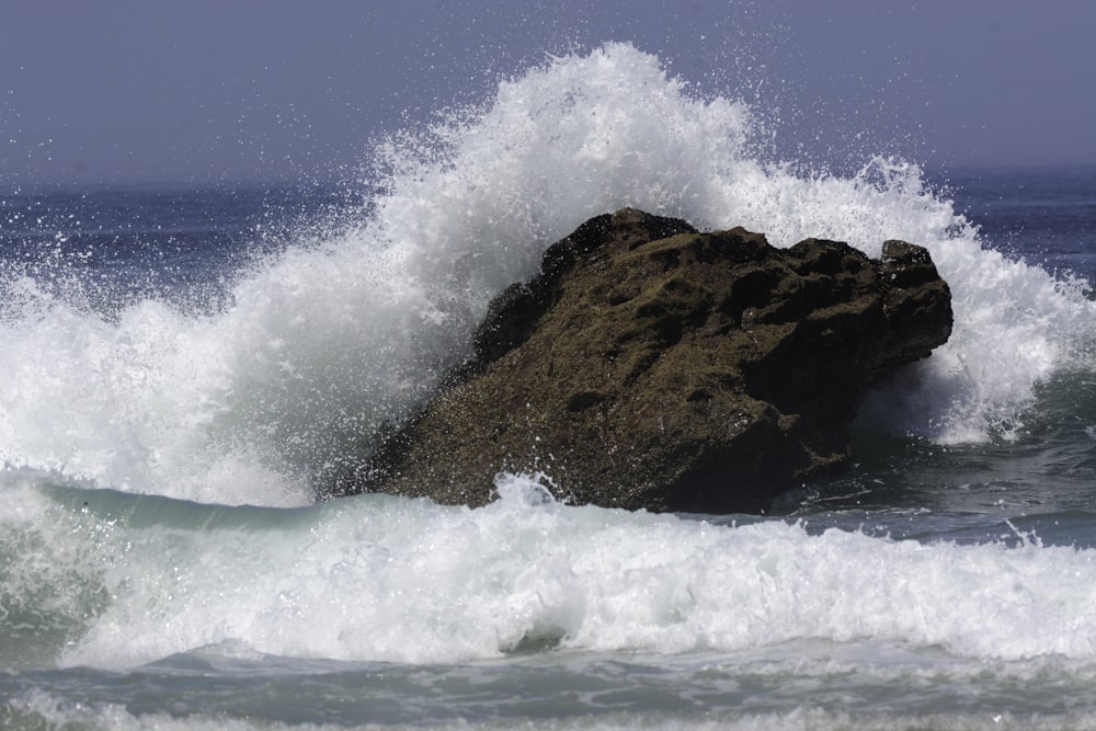 Olas oceánicas rompiendo en la formación rocosa marrón bajo el cielo azul durante el día