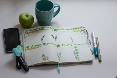 green ceramic mug beside black click pen on white and green book thursday teams background