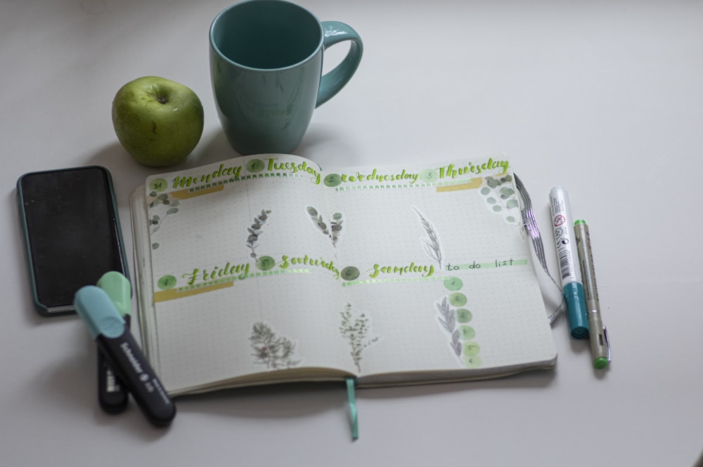 green ceramic mug beside black click pen on white and green book