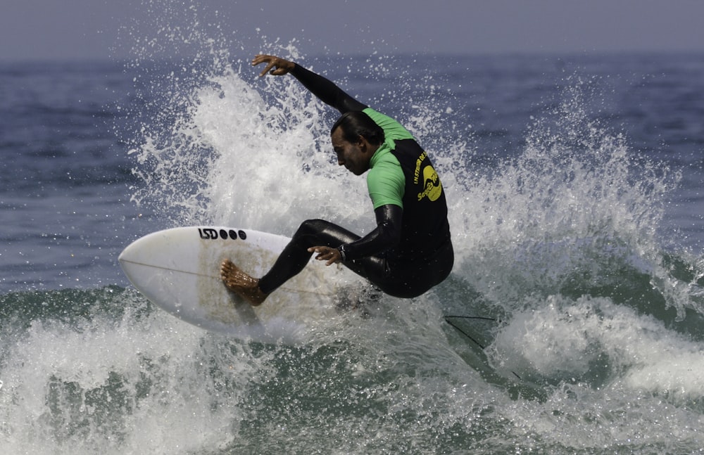 Hombre en traje de neopreno verde y negro surfeando en las olas del mar durante el día