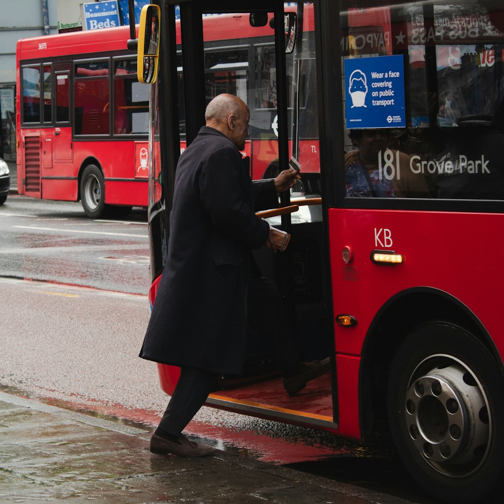 man in black coat standing beside red bus during daytime