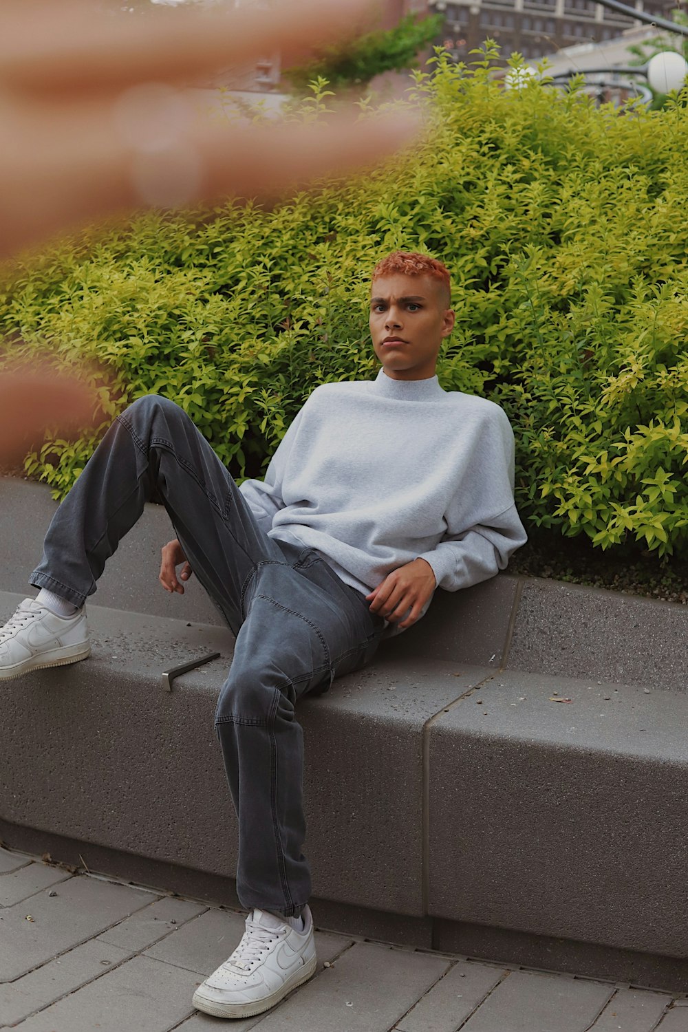 Hombre en suéter blanco sentado en un banco de concreto gris