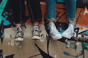 Two people in jeans wearing black and light blue sneakers against a graffiti wall
