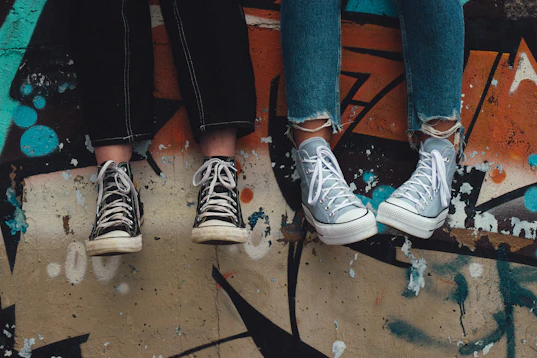 Two people in jeans wearing black and light blue sneakers against a graffiti wall