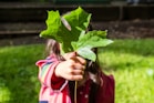 girl in pink jacket holding green maple leaf