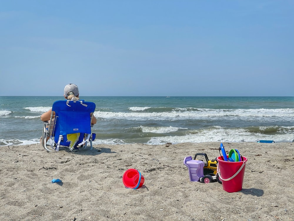 man in blue shirt sitting on blue camping chair on beach during daytime