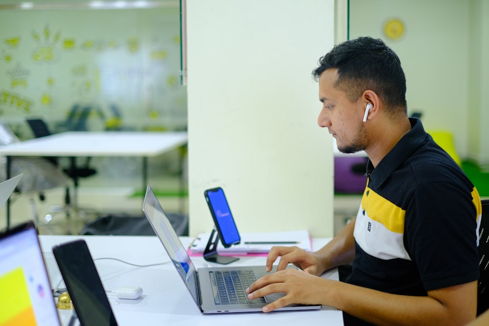 man in black and yellow polo shirt using macbook pro