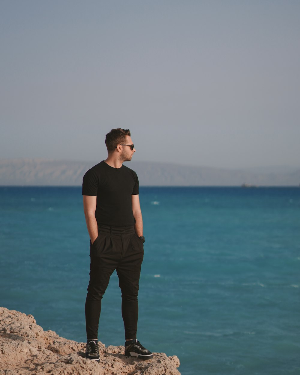 woman in black tank top and brown pants standing on brown rock near body of water