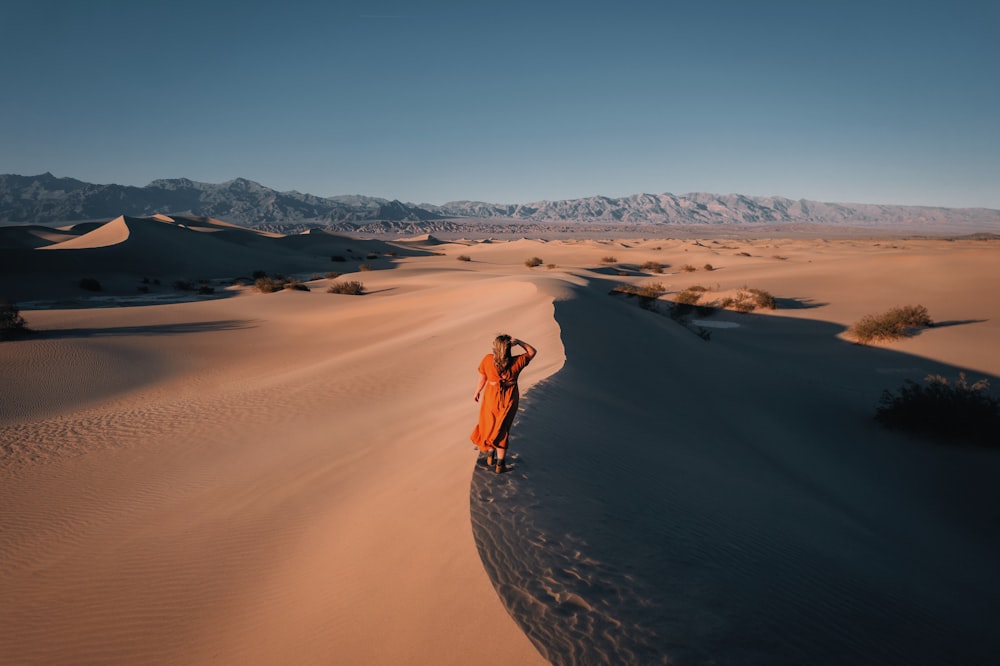 Person in brauner Jacke, die tagsüber auf braunem Sand spazieren geht