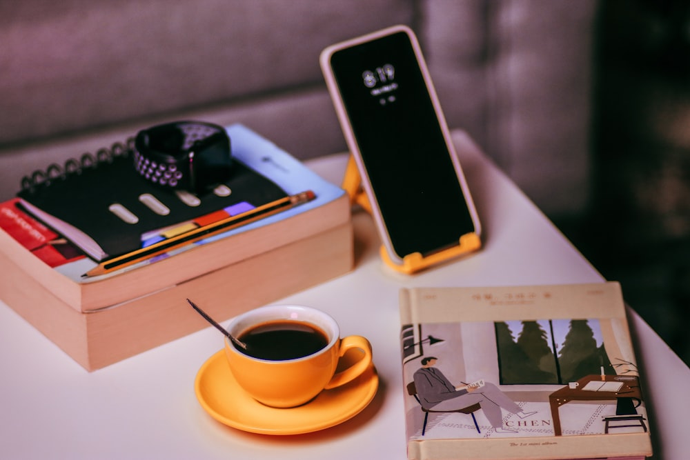 black iphone 5 on white book beside coffee cup with saucer