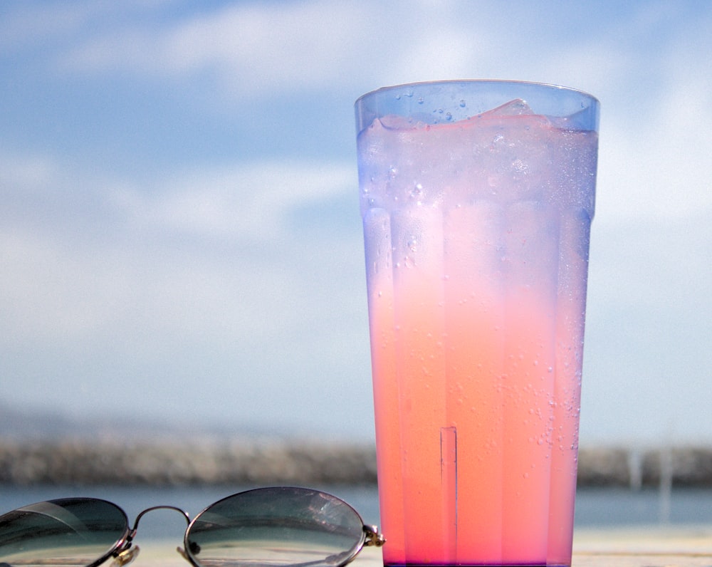 gafas de montura negra junto a un vaso transparente con líquido rosa