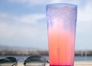 black framed eyeglasses beside clear drinking glass with pink liquid