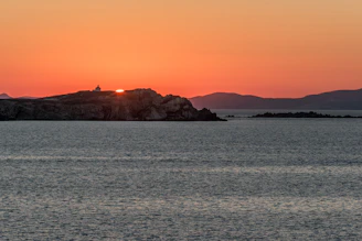 A warm sunset over a serene Greek island coastline with gentle waves and vibrant colors.