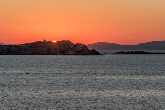 A warm sunset over a serene Greek island coastline with gentle waves and vibrant colors.