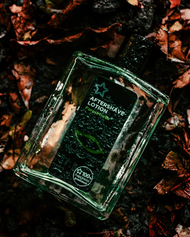 A bottle of musky forest fragrance resting on a bed of fallen leaves at dawn.