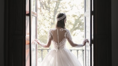 woman in white wedding dress standing near window during daytime