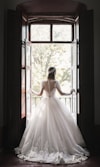 woman in white wedding dress standing near window during daytime