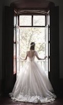 woman in white wedding dress standing near window during daytime