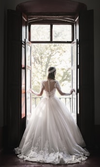 woman in white wedding dress standing near window during daytime