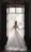 A woman in an elaborate, lace-embroidered wedding dress stands in front of an open window, looking outside. The dress features a full skirt and long sleeves with intricate lace detailing. Sunlight filters through the window, casting a soft glow around her.