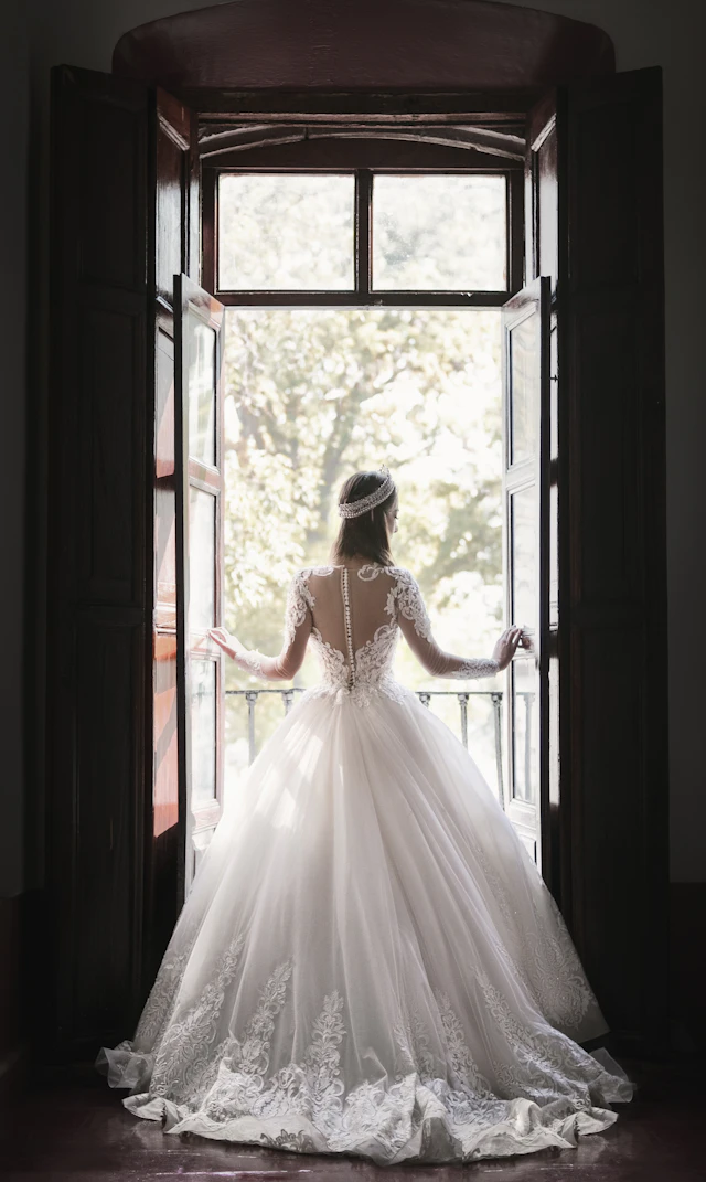 Novia de espaldas frente a una ventana abierta, con vestido de encaje