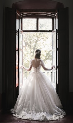 woman in white wedding dress standing near window during daytime