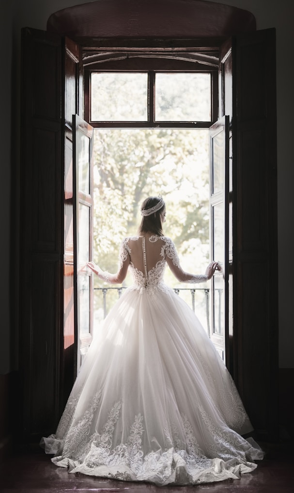 woman in white wedding dress standing near window during daytime