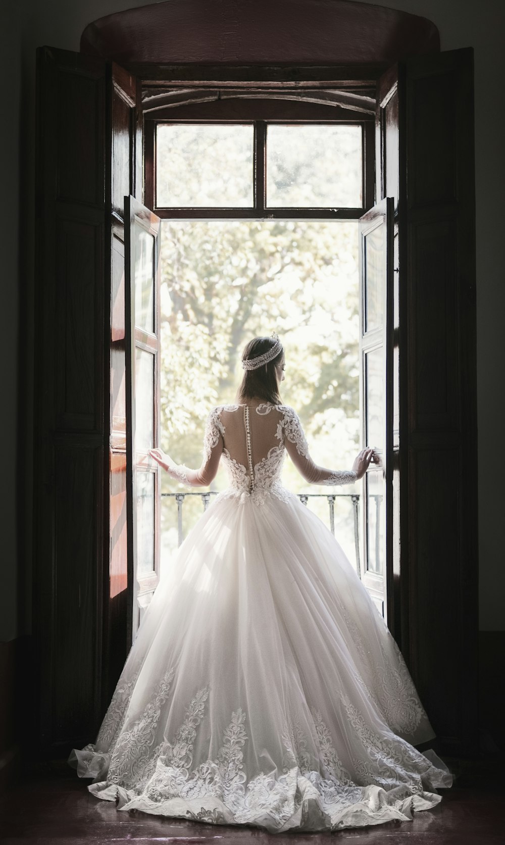 donna in abito da sposa bianco in piedi vicino alla finestra durante il giorno