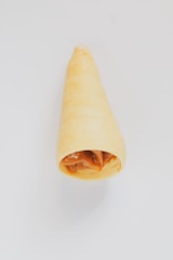 A pastry cone filled with caramel or a similar brown filling, displayed against a plain white background, highlighting its texture and color.