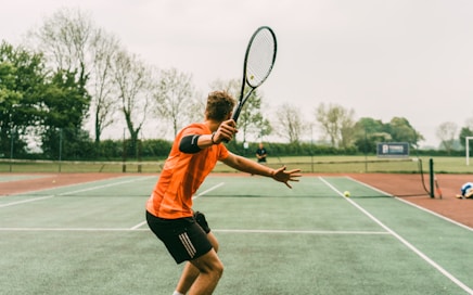 man in orange shirt and black shorts holding black and white tennis racket