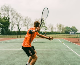 man in orange shirt and black shorts holding black and white tennis racket