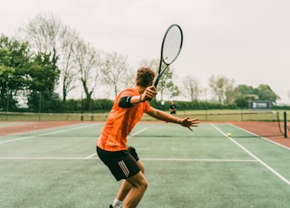 man in orange shirt and black shorts holding black and white tennis racket