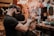 A barber is giving a haircut to a client in a stylish and colorful barbershop. The barber, wearing a black cap and t-shirt, focuses intently as he uses scissors to trim the client's hair. The shop's walls are adorned with vibrant graffiti art and various decorations, adding to the lively atmosphere.