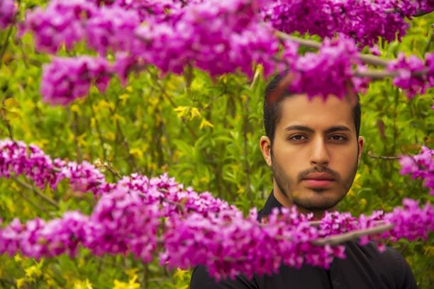 A young man working on a beautifully landscaped garden with vibrant flowers and lush greenery.