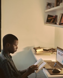 A student happily studying with a laptop and books in a cozy home setting.