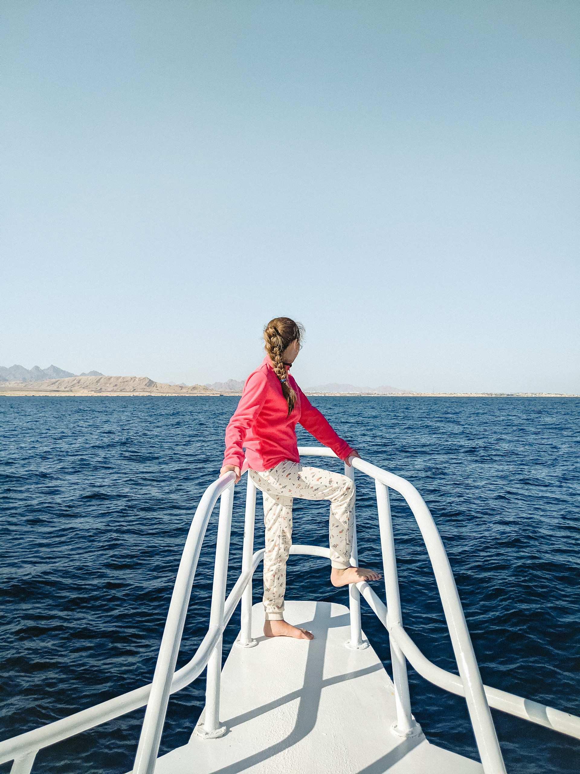 woman in red dress standing on white metal railings near body of water during daytime