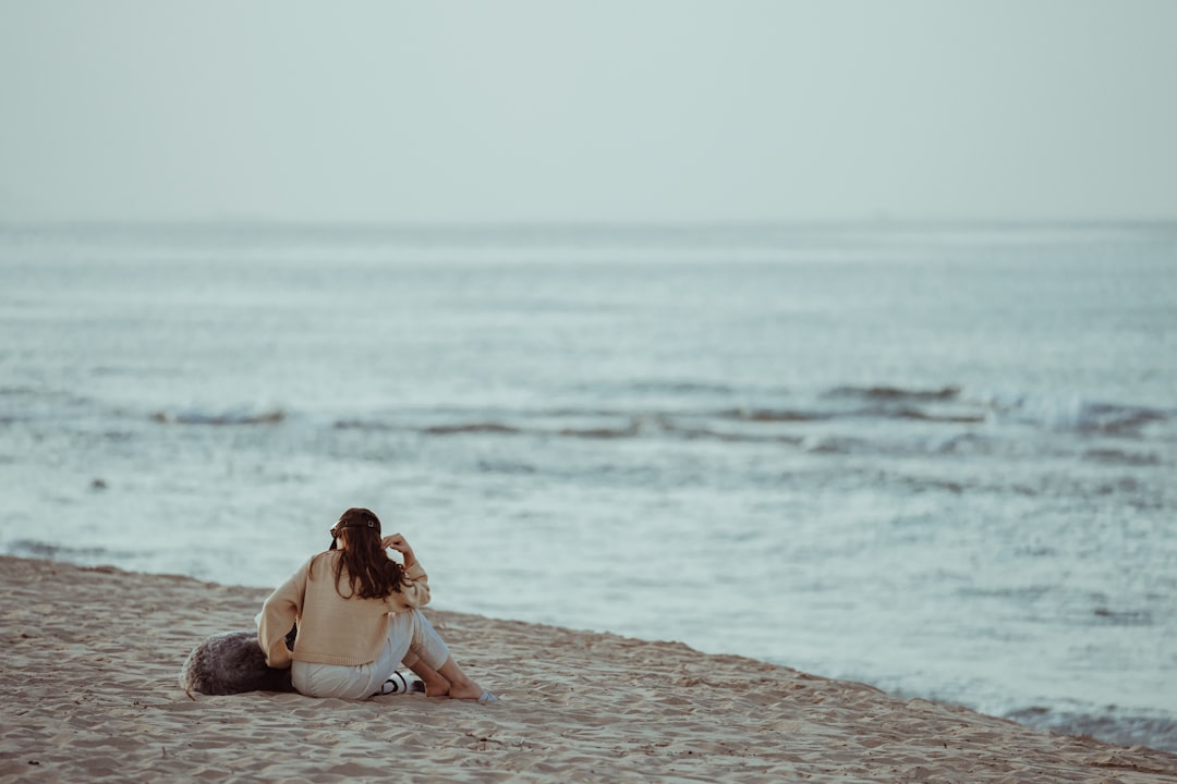 woman in white dress sitting on brown concrete floor near sea during daytime