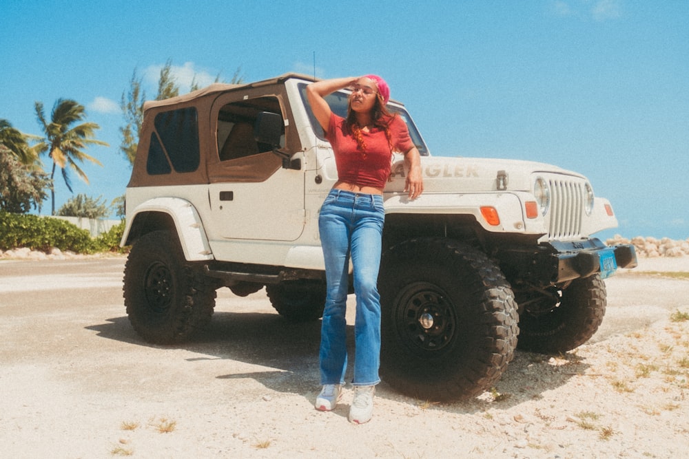 man in red shirt and blue denim jeans standing beside white suv during daytime