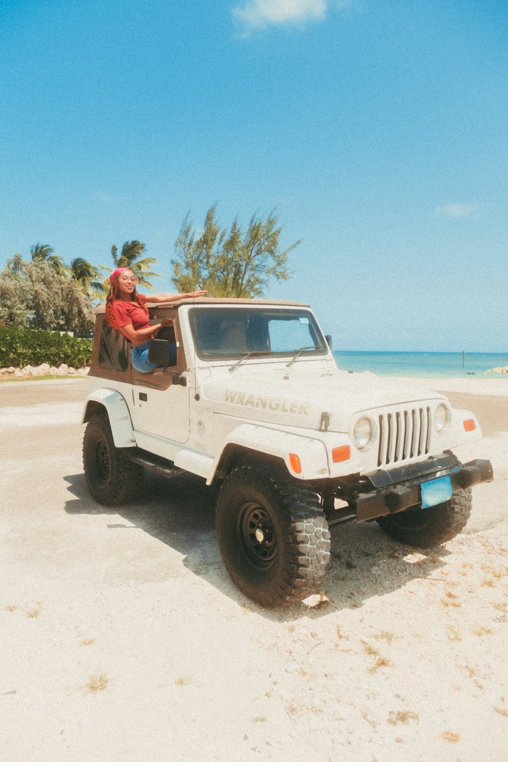 man in brown shirt sitting on white jeep wrangler on beach during daytime