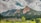A stunning landscape featuring rugged, angled rock formations known as the Flatirons, rising majestically against a backdrop of a cloudy sky. Lush green trees and grass cover the foreground, providing a stark contrast to the rocky mountains.