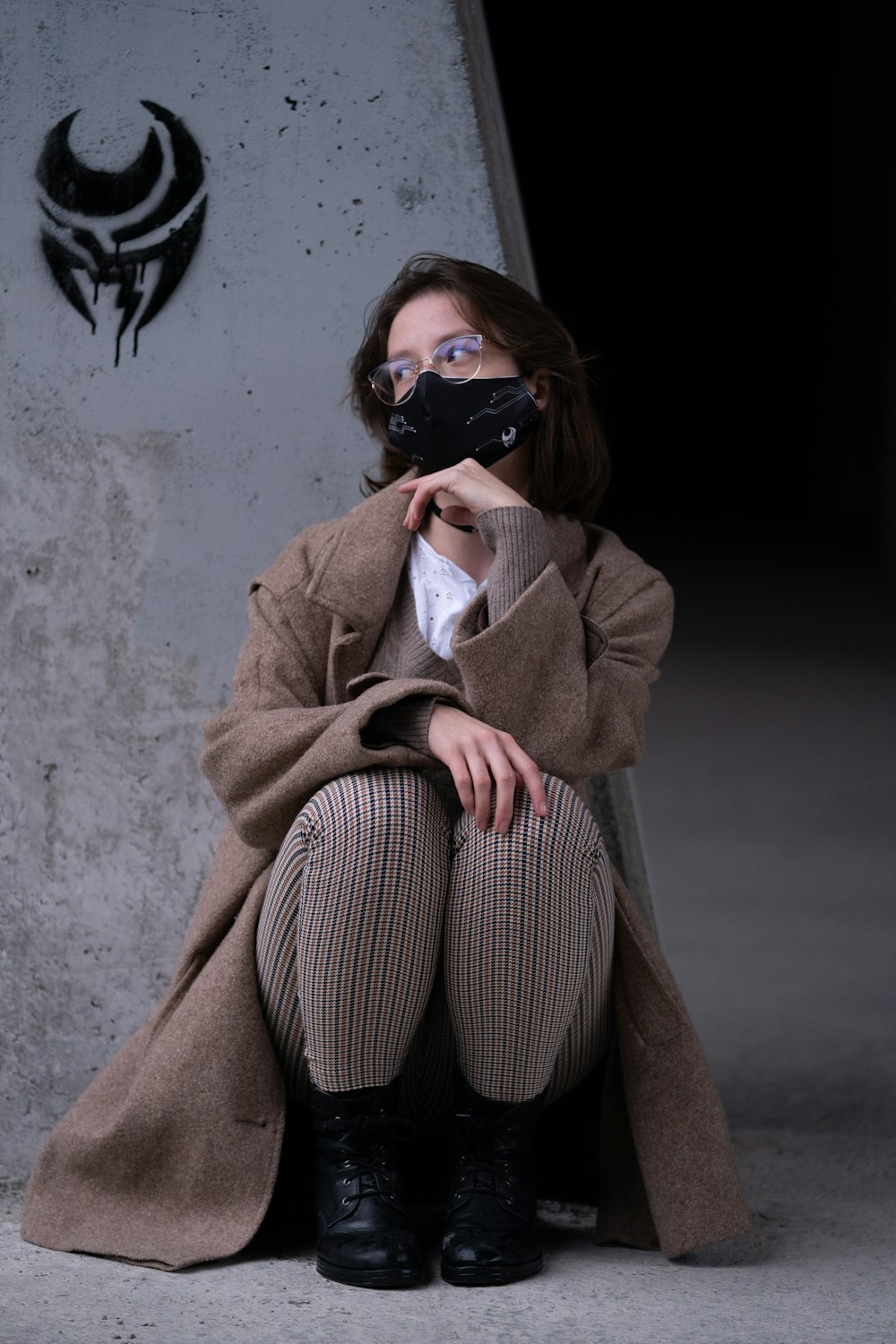 woman in brown coat and brown pants sitting on gray concrete wall