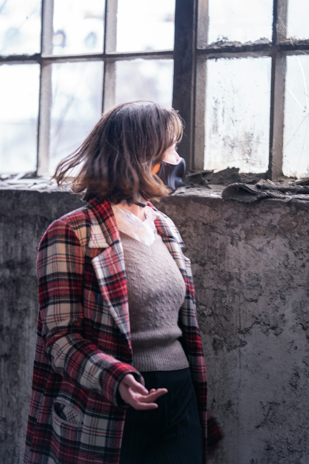 woman in red and black plaid coat standing near window during daytime