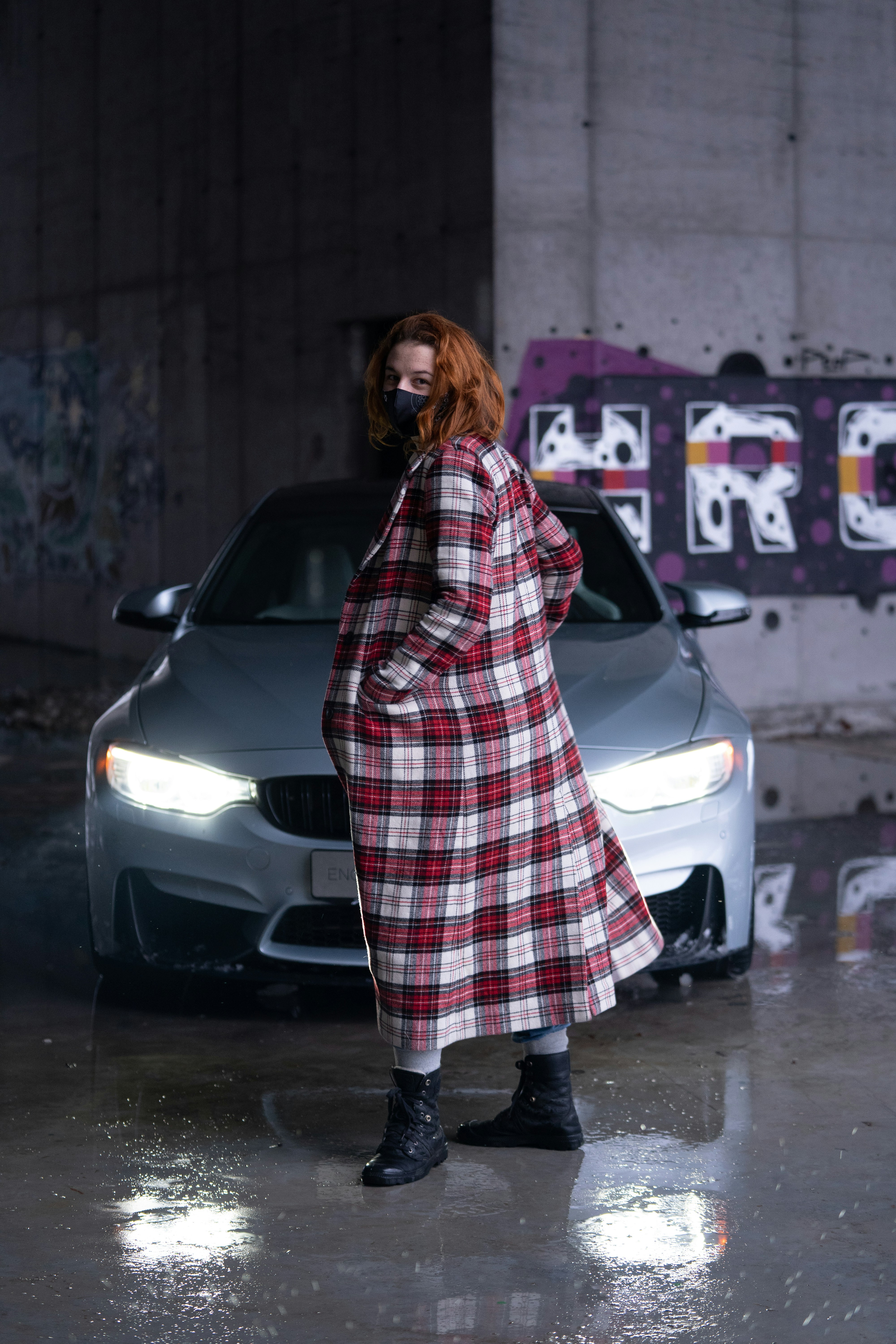 woman in black and white plaid coat standing beside white car