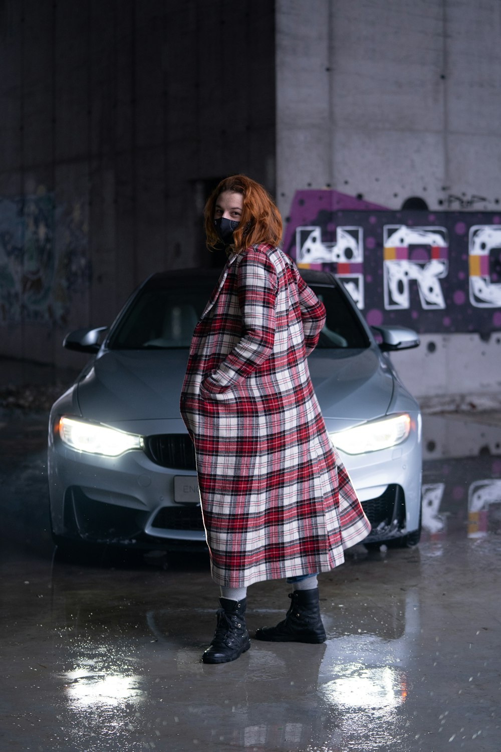 woman in black and white plaid coat standing beside white car