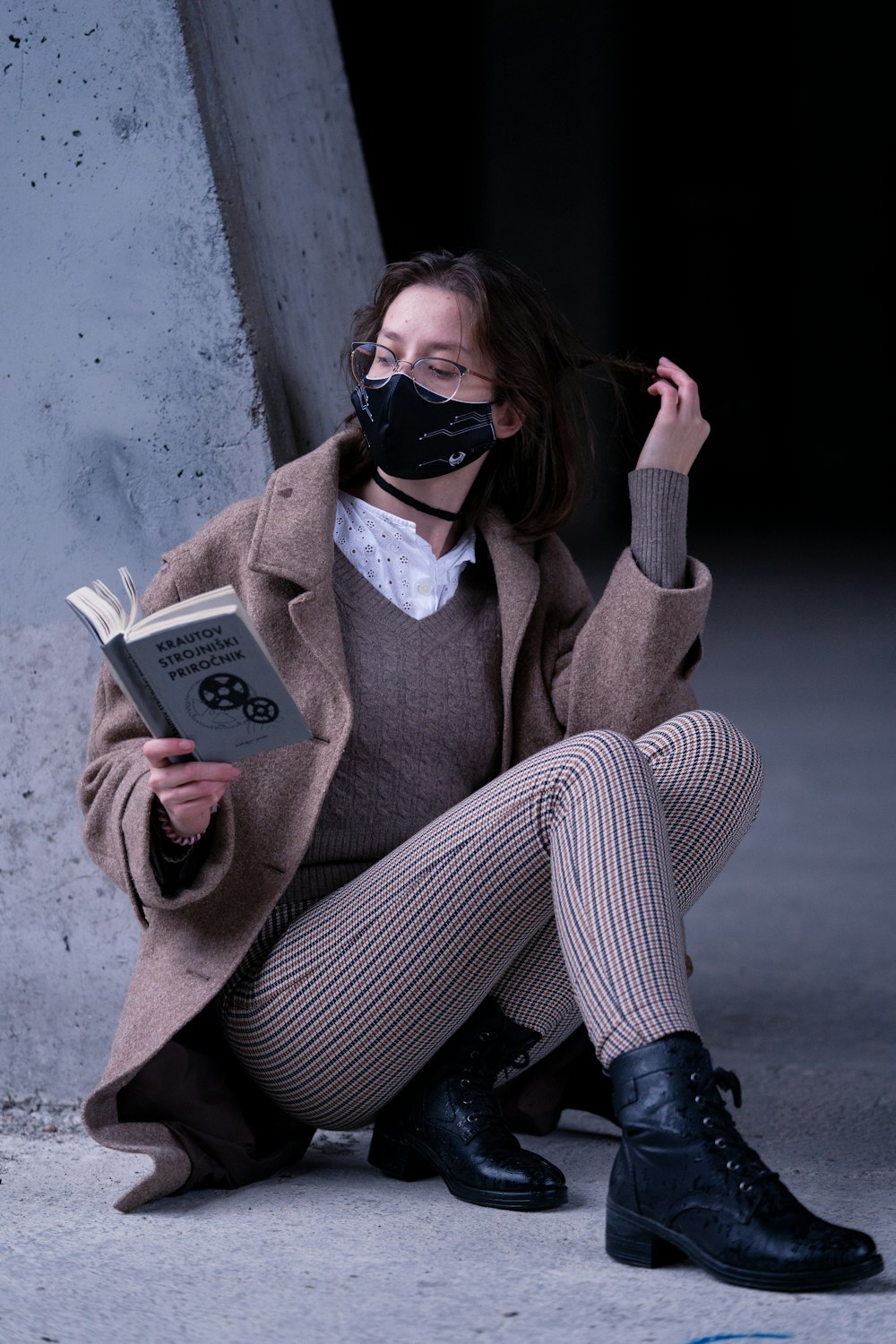 woman in brown coat wearing black goggles holding white book