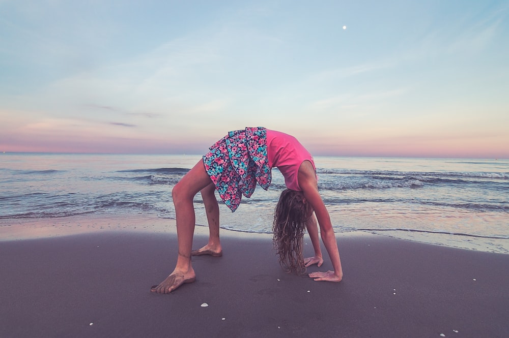 woman in pink shirt and blue and white floral skirt standing on beach during daytime